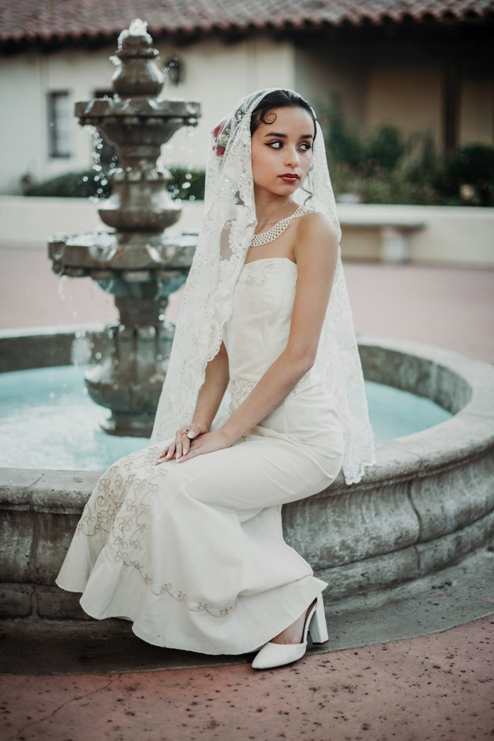 a woman in a wedding dress sitting in front of a fountain