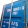 A close-up view of a blue shipping container door displaying white text with serial numbers and weight specifications. The metal bolts and latches are visible, adding a rugged aspect to the industrial container.