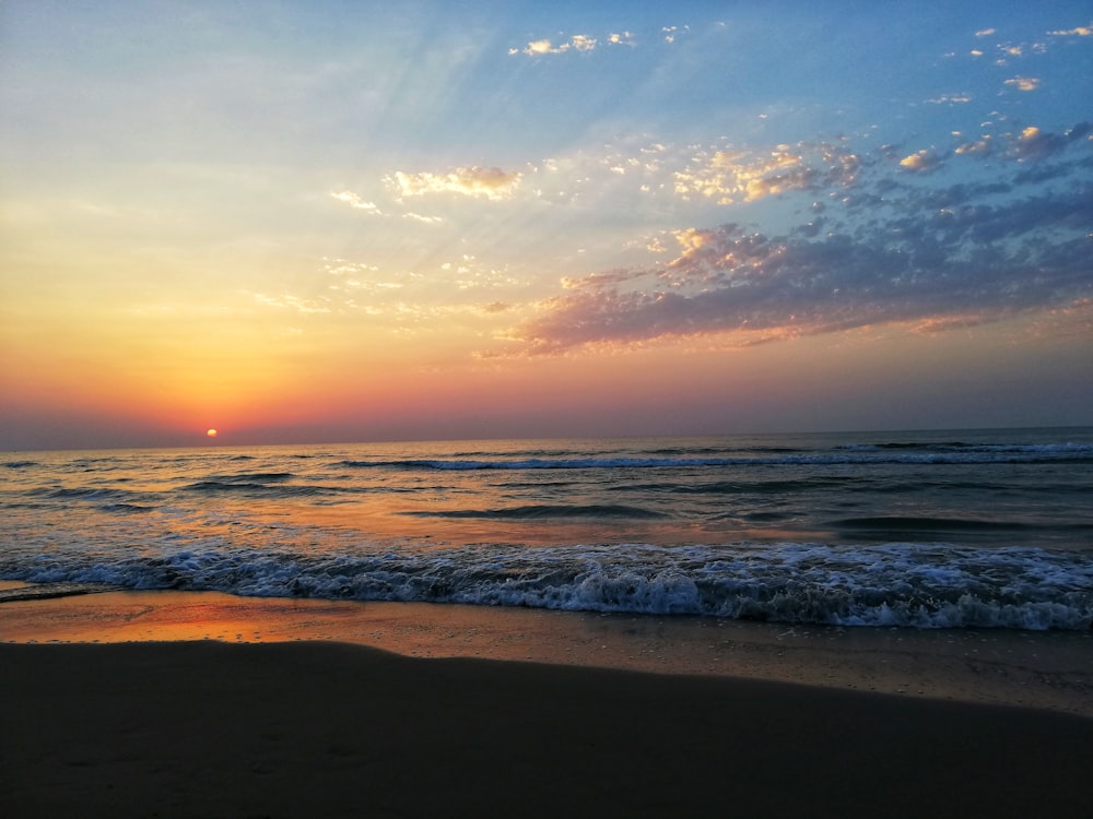 the sun is setting over the ocean on the beach