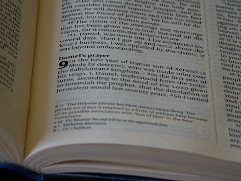A close-up view of an open Bible, focusing on the text from the book of Daniel. The visible passage discusses Daniel's prayer during the first year of Darius's reign. The page has notes at the bottom providing additional context or translation details.
