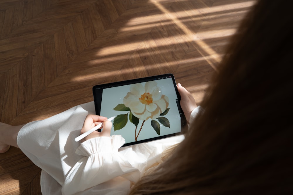 a woman is holding a tablet with a picture of a flower on it