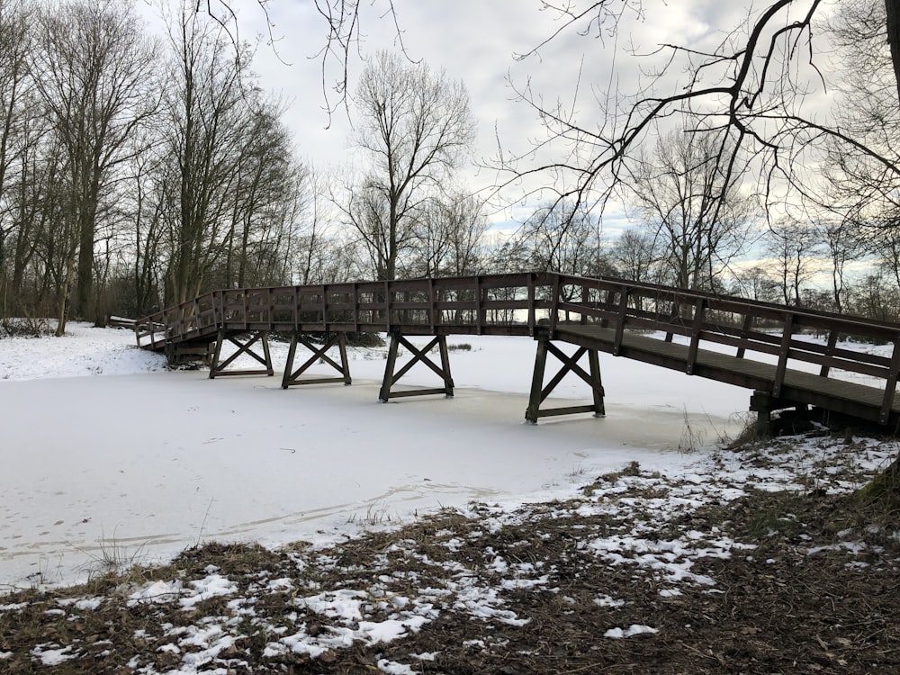 a wooden bridge over snow covered ground next to trees