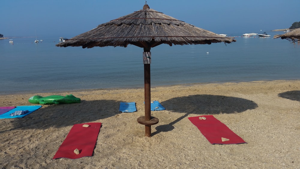 a beach with a straw umbrella and red mats