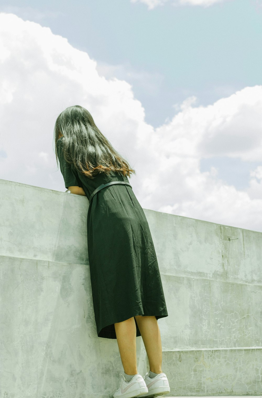 a woman in a green dress leaning against a wall