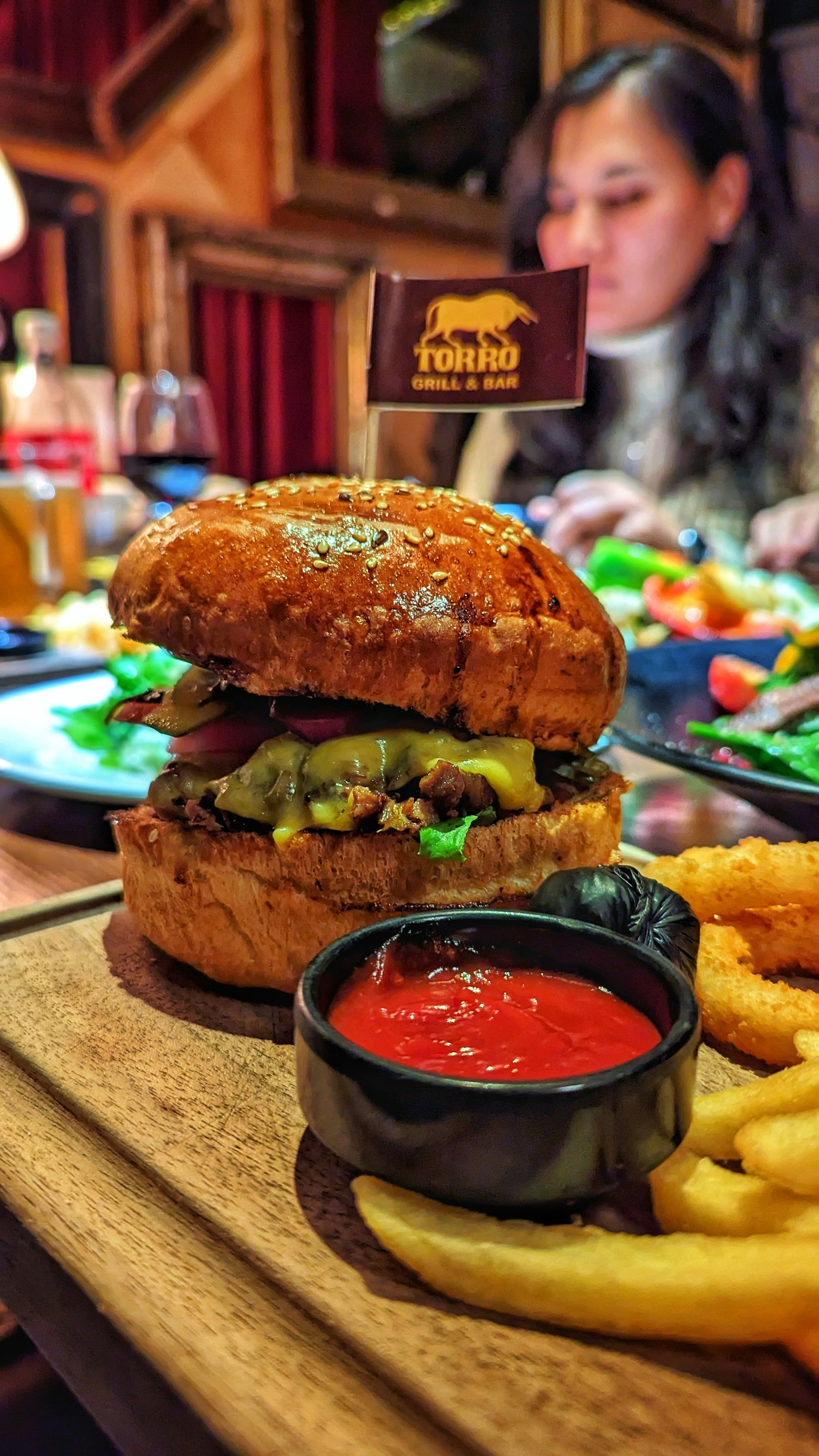 BBQ burger with smoky sauce and onion rings on wooden board