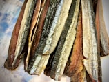 Several strips of dried fish with a shiny, silvery skin and a brownish interior texture are arranged closely together, creating a layered effect.