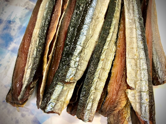 Several strips of dried fish with a shiny, silvery skin and a brownish interior texture are arranged closely together, creating a layered effect.