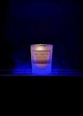 A lit candle with a label that reads 'Only For You, Handmade Candle, Aromatherapy Experts' is placed against a dark background. The candle emits a soft, warm glow surrounded by a subtle blue mist or smoke.