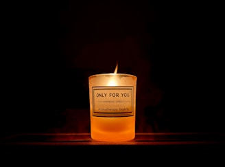 A warm, glowing candle with a custom label featuring a Bible verse, set against a cozy wooden background.