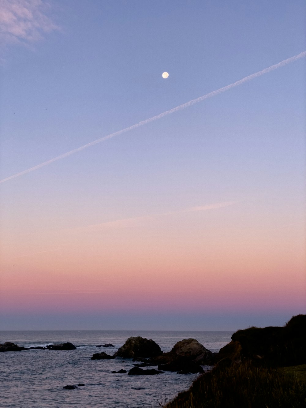 the moon is setting over the ocean and rocks