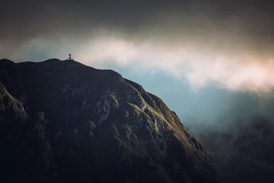 A misty mountain peak at dawn with a lone hiker silhouetted against the sky.