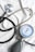 A stethoscope and a sphygmomanometer are laid out on a white fabric surface. The stethoscope has a shiny metallic diaphragm and black tubing. The sphygmomanometer features a round gauge with blue, red, and black markings indicating blood pressure measurements, attached to a gray and black bulb used for inflating the cuff.