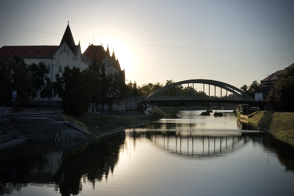 the sun is setting over a river with a bridge in the background