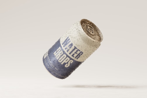 A water can is suspended in mid-air. The can has the label 'WATER DROPS' and appears to be covered in condensation or droplets, giving a refreshing and cool appearance. The background is a plain, light color, emphasizing the can.