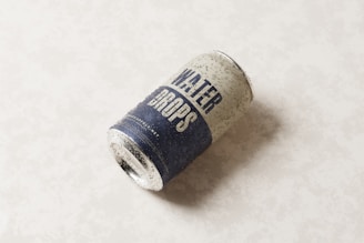 A can labeled 'water drops' is lying on its side on a light background. The can appears to be cold or recently taken out of a refrigerator, with visible condensation forming small droplets on its surface.