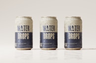 Three beverage cans covered in condensation are aligned in a row against a light, neutral background. The cans are labeled with the words 'Water Drops' in bold blue letters on a white background, with additional text and a QR code near the bottom.
