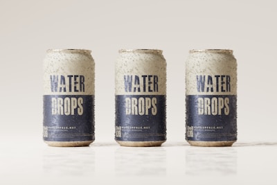 Three beverage cans covered in condensation are aligned in a row against a light, neutral background. The cans are labeled with the words 'Water Drops' in bold blue letters on a white background, with additional text and a QR code near the bottom.
