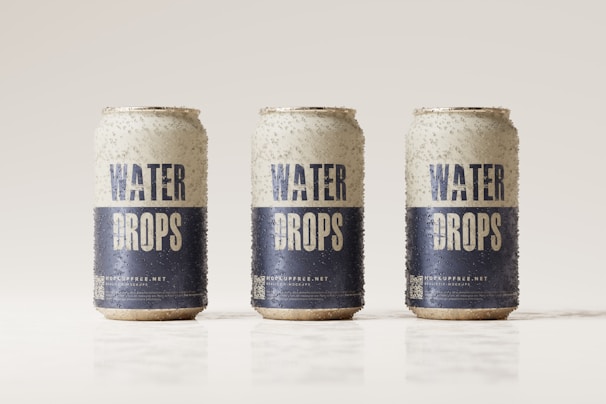 Three beverage cans covered in condensation are aligned in a row against a light, neutral background. The cans are labeled with the words 'Water Drops' in bold blue letters on a white background, with additional text and a QR code near the bottom.