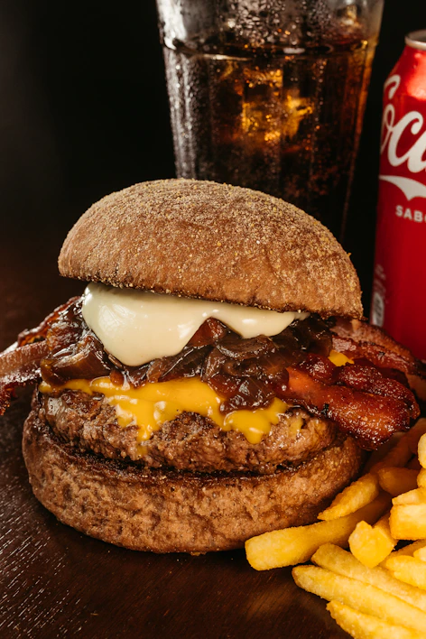 Close-up of a juicy classic burger with golden fries and a cold soda on the side.