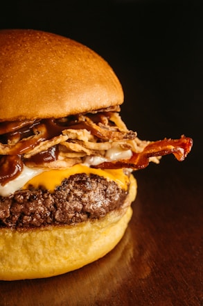 A close-up of a gourmet hamburger featuring a juicy beef patty topped with melted cheese, crispy bacon, fried onion strings, and rich barbecue sauce, all sandwiched between a soft, toasted bun.