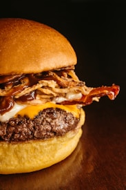 A close-up of a gourmet hamburger featuring a juicy beef patty topped with melted cheese, crispy bacon, fried onion strings, and rich barbecue sauce, all sandwiched between a soft, toasted bun.