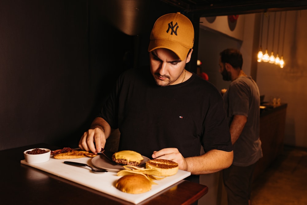 a man in a yellow hat is cutting a sandwich