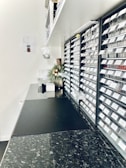 A sleek, modern workspace with a long black countertop. Numerous labeled compartments are neatly organized along the wall, possibly for filing or storage purposes. The setting includes some decorative elements like a small plant arrangement, creating a minimalistic and organized vibe.