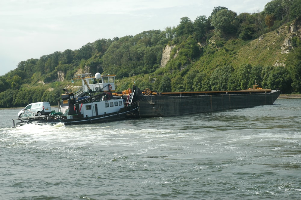 a large boat traveling down a river next to a lush green hillside