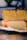 A loaf of freshly baked bread is sliced to reveal a soft, airy crumb. The top of the bread is covered with a variety of seeds, adding texture and flavor. The bread is resting on a cooling rack with a piece of parchment paper underneath.