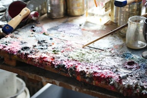 An artist working on a large canvas, surrounded by brushes and paint palettes.