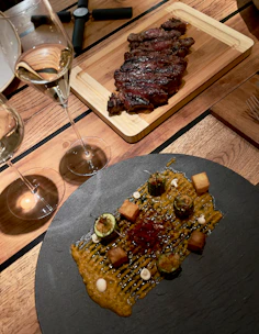 Elegant glass of red wine beside a plate of grilled steak, set on a dark wood table.