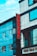 A street view of a modern building featuring a vertical red sign with the letters 'ROHAN ACC.' The building is composed of blue and gray panels with multiple windows. Power lines crisscross the scene, and part of a sign with 'GEE ESS F' is visible at the bottom.