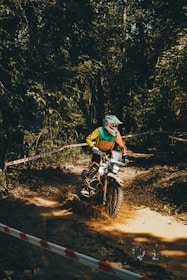 A rugged motocross track winding through dense forest with jumps and sharp turns.