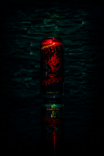 A red energy drink can with bold, fiery graphics and text, set against a dark textured background. The can is reflected below, creating a mirrored effect.