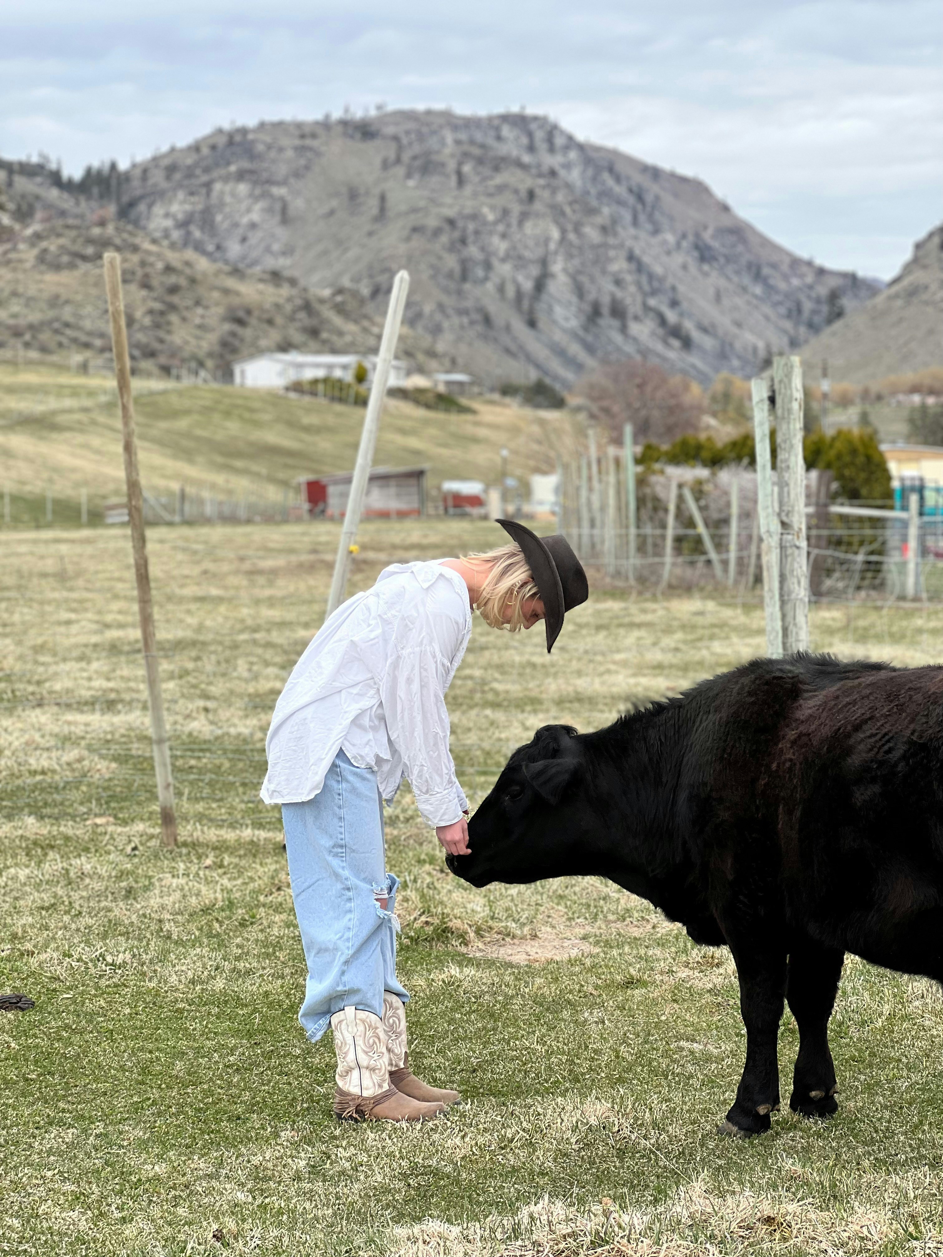 a man standing next to a black cow on a lush green field
