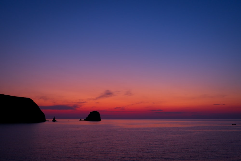 a sunset over a body of water with a rock outcropping in the