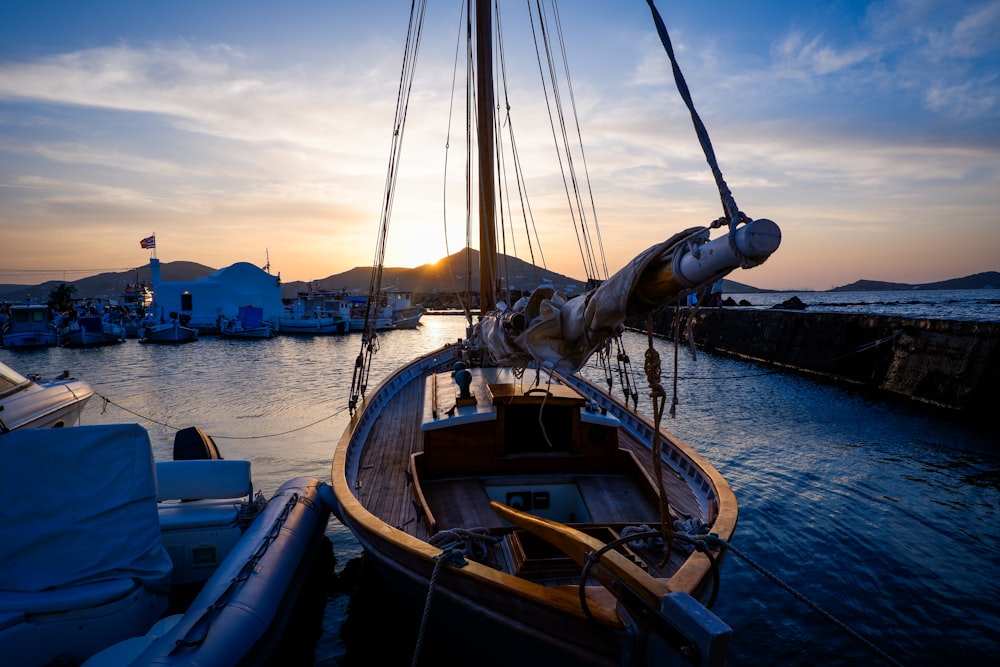 a sailboat docked at a dock with the sun setting in the background