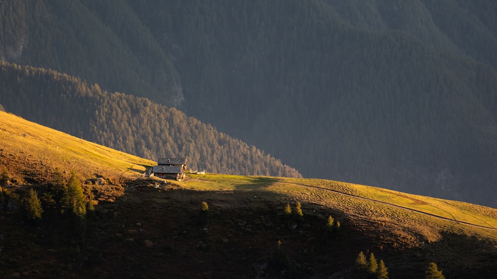 Une maison isolée sur une colline herbeuse avec des montagnes en arrière-plan