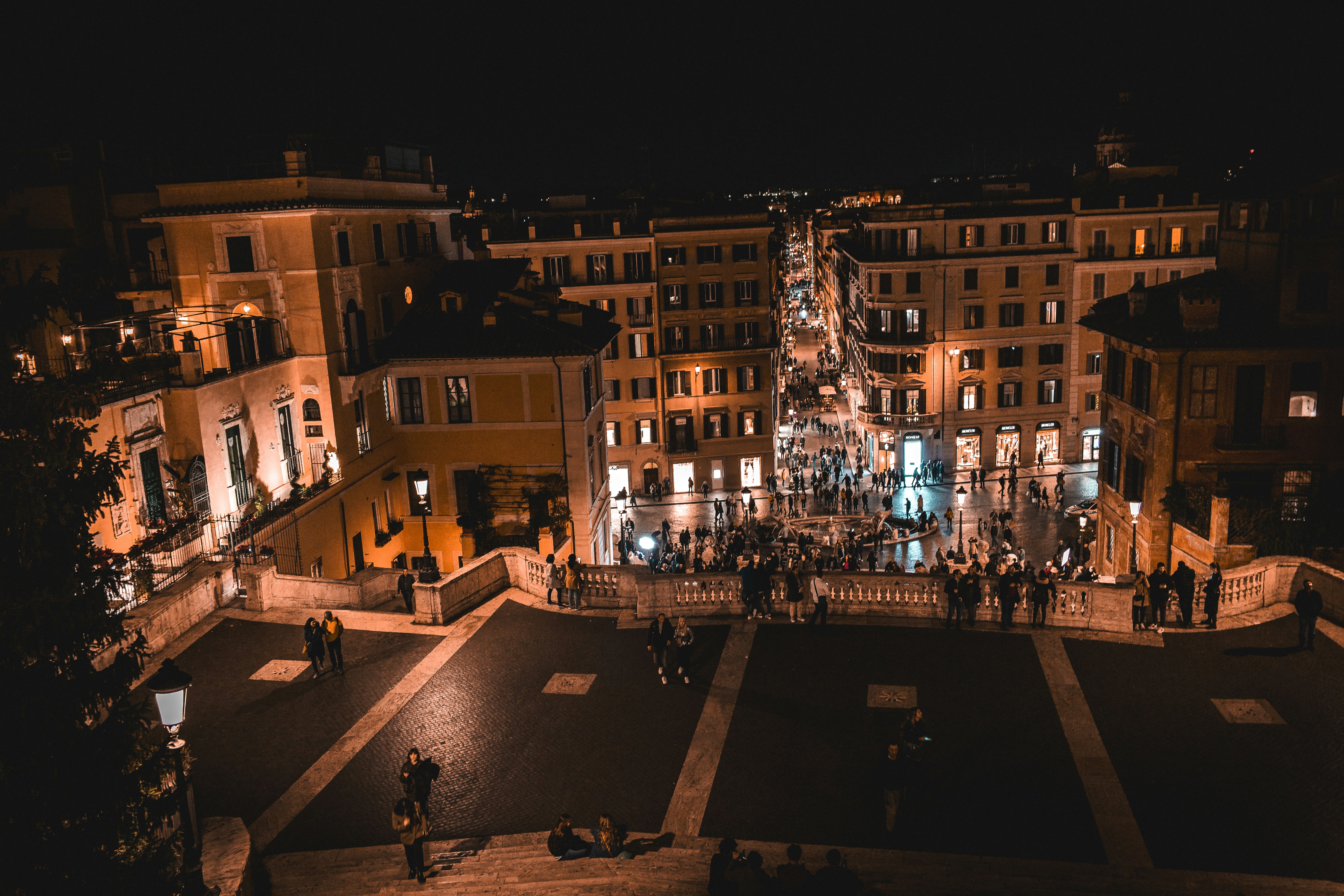 a group of people standing around a plaza at night, 