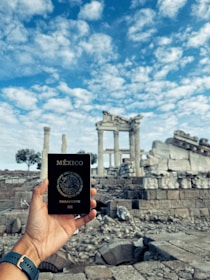 a person holding up a passport in front of ruins
