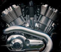 A close-up view of a motorcycle engine with metallic parts and reflective surfaces. The image highlights the intricate design of the engine components, including the cylinders, pipes, and various bolts.