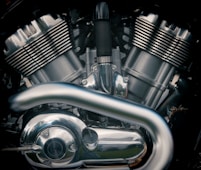 A close-up view of a motorcycle engine with metallic parts and reflective surfaces. The image highlights the intricate design of the engine components, including the cylinders, pipes, and various bolts.
