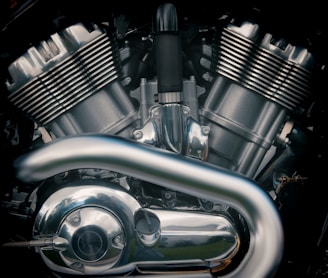 A close-up view of a motorcycle engine with metallic parts and reflective surfaces. The image highlights the intricate design of the engine components, including the cylinders, pipes, and various bolts.