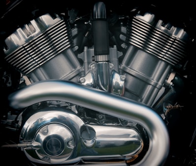 A close-up view of a motorcycle engine with metallic parts and reflective surfaces. The image highlights the intricate design of the engine components, including the cylinders, pipes, and various bolts.