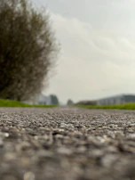 Detailed view of gravel being spread evenly over a roadbed under bright daylight.