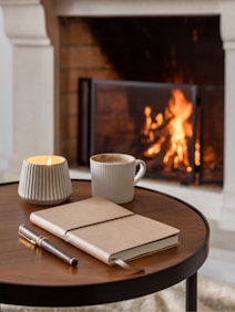 a cup of coffee and a notebook on a table in front of a fireplace