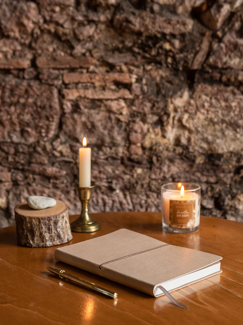 A notebook and a lit candle on a wooden table, set up for an evening journaling routine