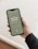 A smartphone displaying a digital journal cover titled 'The New Year Journal' for the years 2023-2024 is being held in a person's hand. The cover has a minimalist design with a greenish background and white text, and the word 'PROPHESEE' at the bottom. The person's hand is visible, showing manicured nails, and they are wearing a dark sweater.