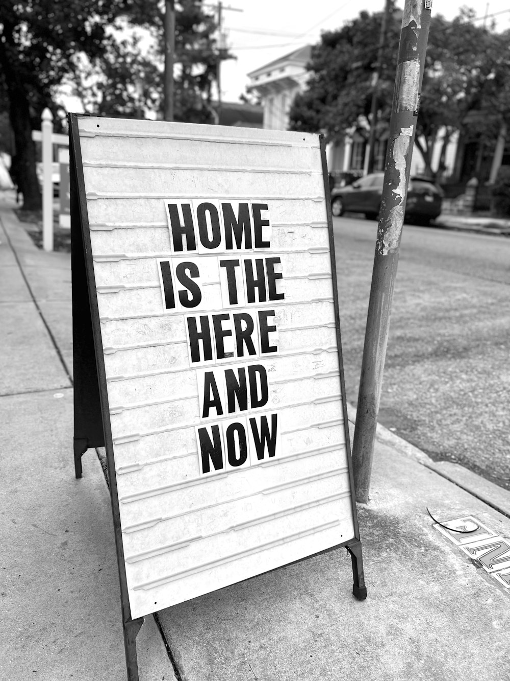 a sign on a sidewalk that says home is the here and now