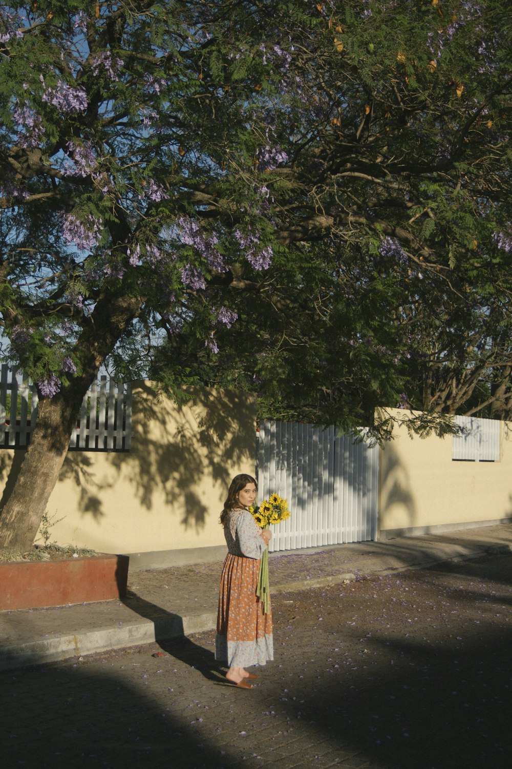 a woman standing under a tree with a bouquet of flowers